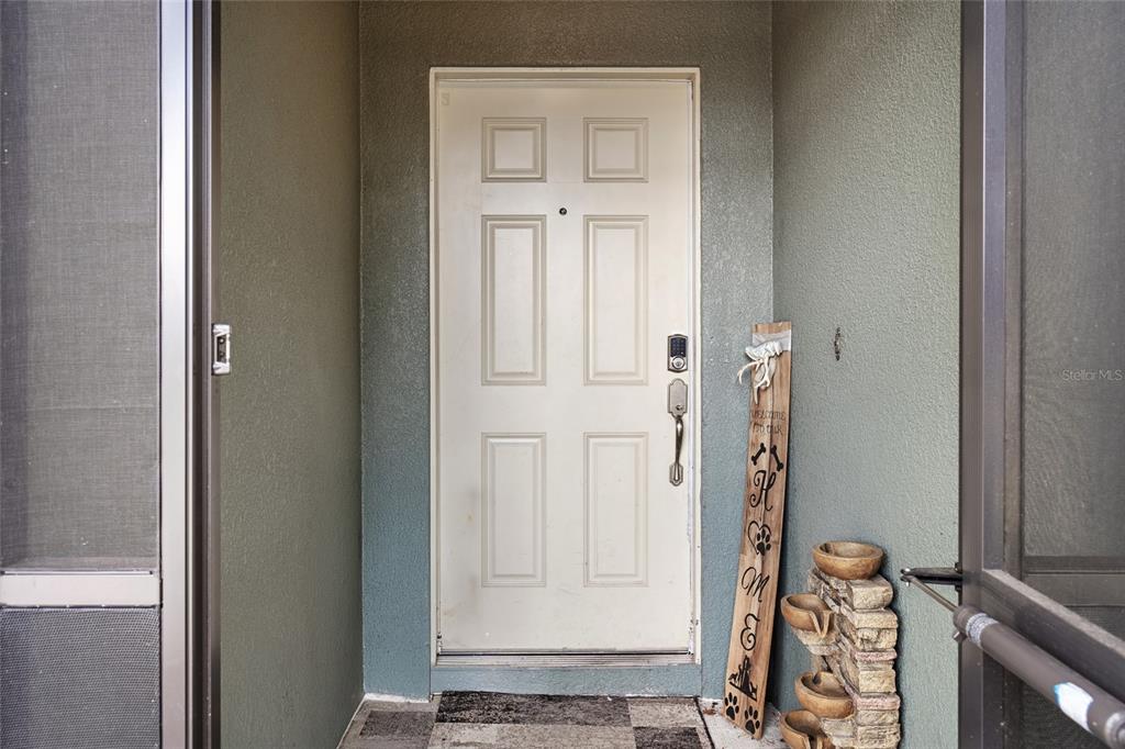 A white front door with a smart lock sits in a covered entryway — 3049 MERLOT WAY, CLERMONT, FL