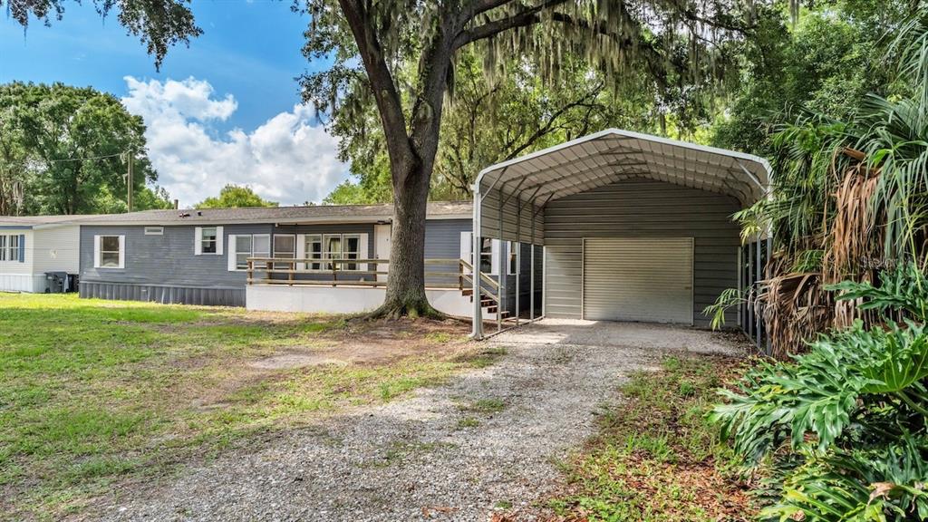 A gray mobile home with a wooden deck and an attached metal carport — 509 SHARON HILL COURT, WINTER HAVEN, FL