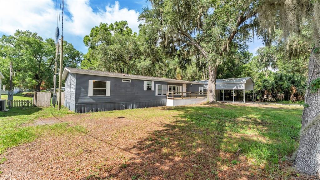 A gray manufactured home with a wooden deck and a metal carport sits on grass — 509 SHARON HILL COURT, WINTER HAVEN, FL