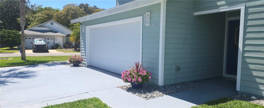 A light blue house exterior features a white garage door, potted flowers, and a driveway — 68 BRISTOL LANE, PALM COAST, FL