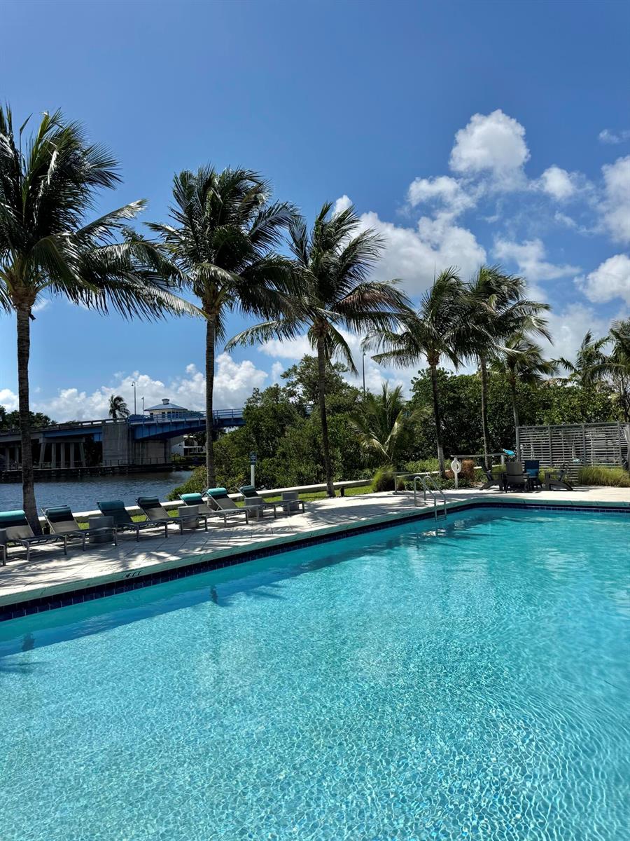 A swimming pool sits beside a patio with lounge chairs, palm trees, and a bridge — 651 E Woolbright Road # 103, Boynton Beach FL 33435, BOYNTON BEACH, FL