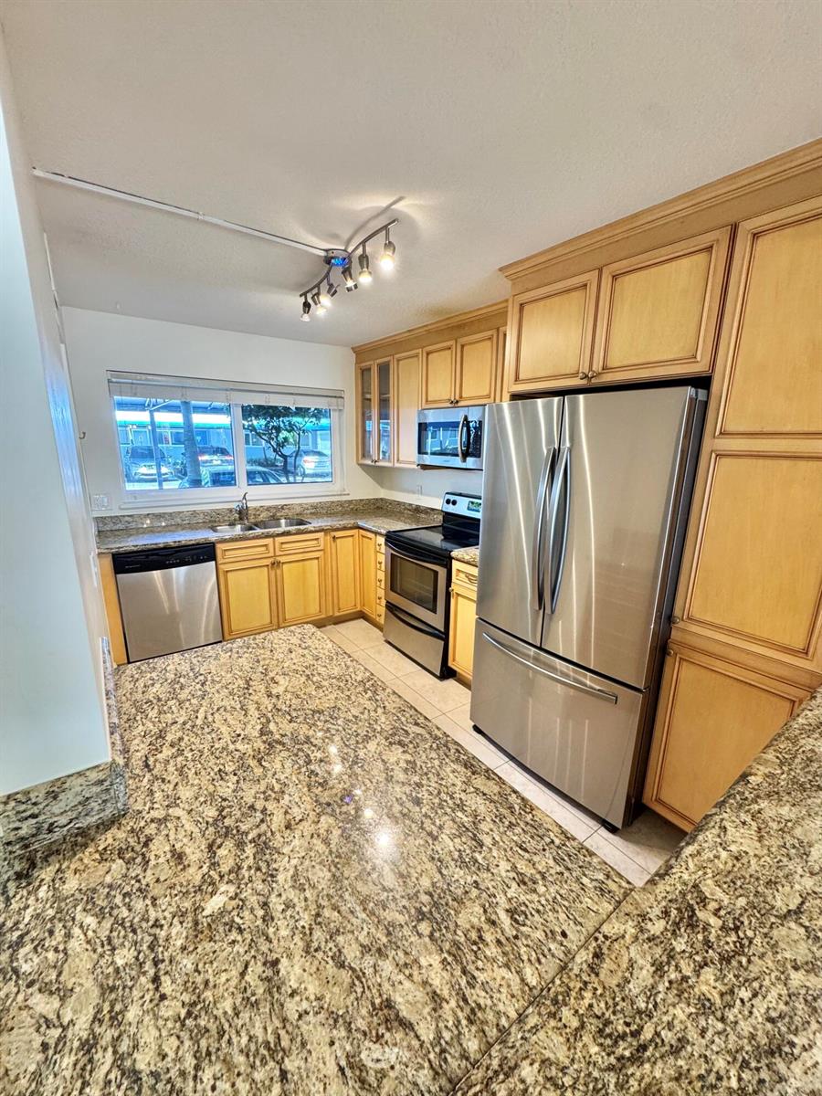 A kitchen features light wood cabinets, granite countertops, stainless steel appliances, and a track light — 651 E Woolbright Road # 103, Boynton Beach FL 33435, BOYNTON BEACH, FL