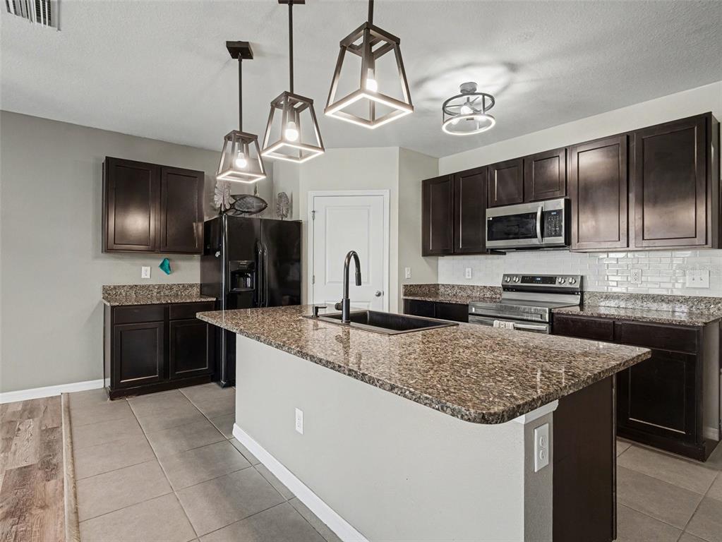 A kitchen features dark wood cabinets, granite countertops, a central island, and stainless steel appliances — 10626 PARK MEADOWBROOKE DRIVE, RIVERVIEW, FL