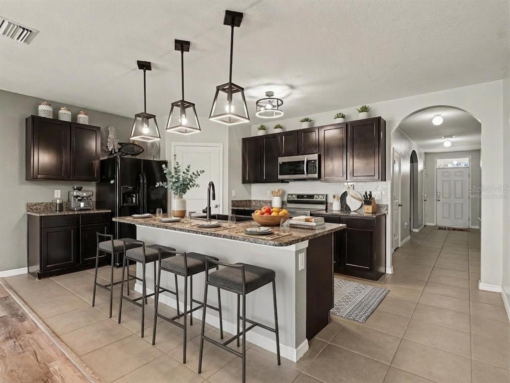 A kitchen features dark wood cabinets, granite countertops, a central island, and three pendant lights — 10626 PARK MEADOWBROOKE DRIVE, RIVERVIEW, FL