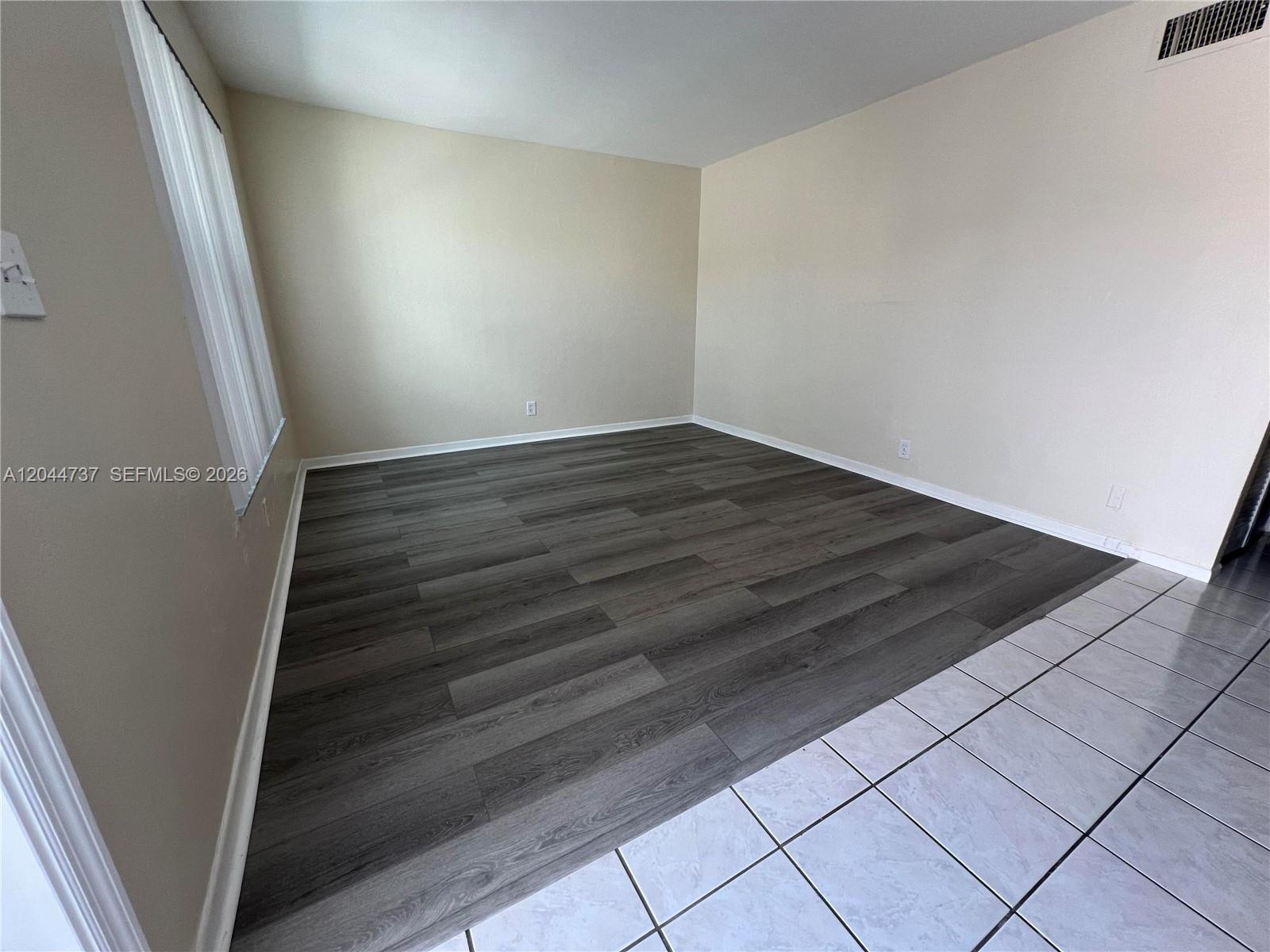 An empty room features dark wood-look flooring, light walls, and a white tiled entryway — 3745 SW 59th Ave # 124, Davie FL 33314, DAVIE, FL