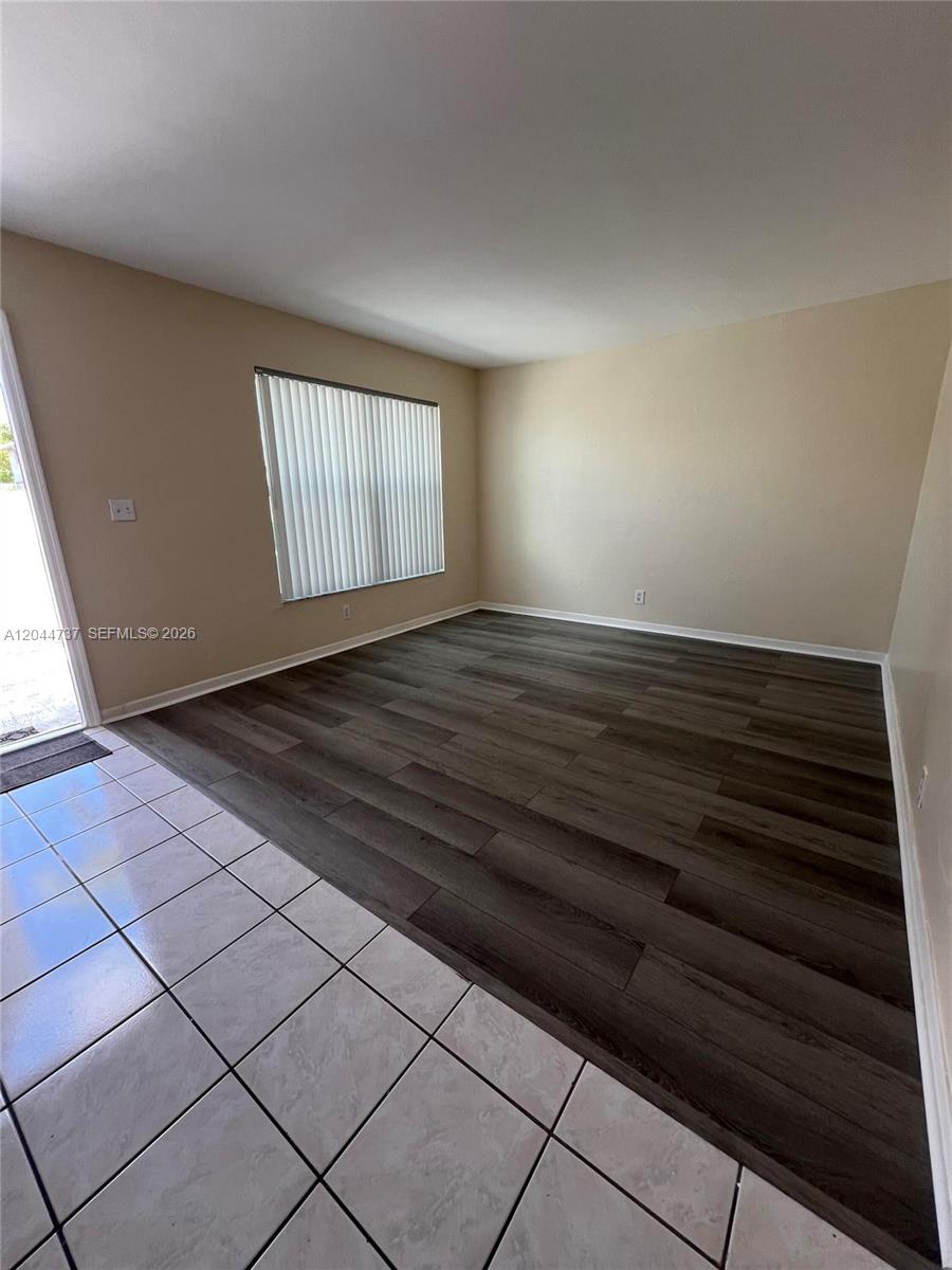 An empty room features dark wood-look flooring, light-colored walls, and a large window with blinds — 3745 SW 59th Ave # 124, Davie FL 33314, DAVIE, FL