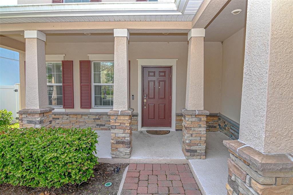 A covered front porch with stone-based columns leads to a red front door — 5973 CYPRESS HILL ROAD, WINTER GARDEN, FL