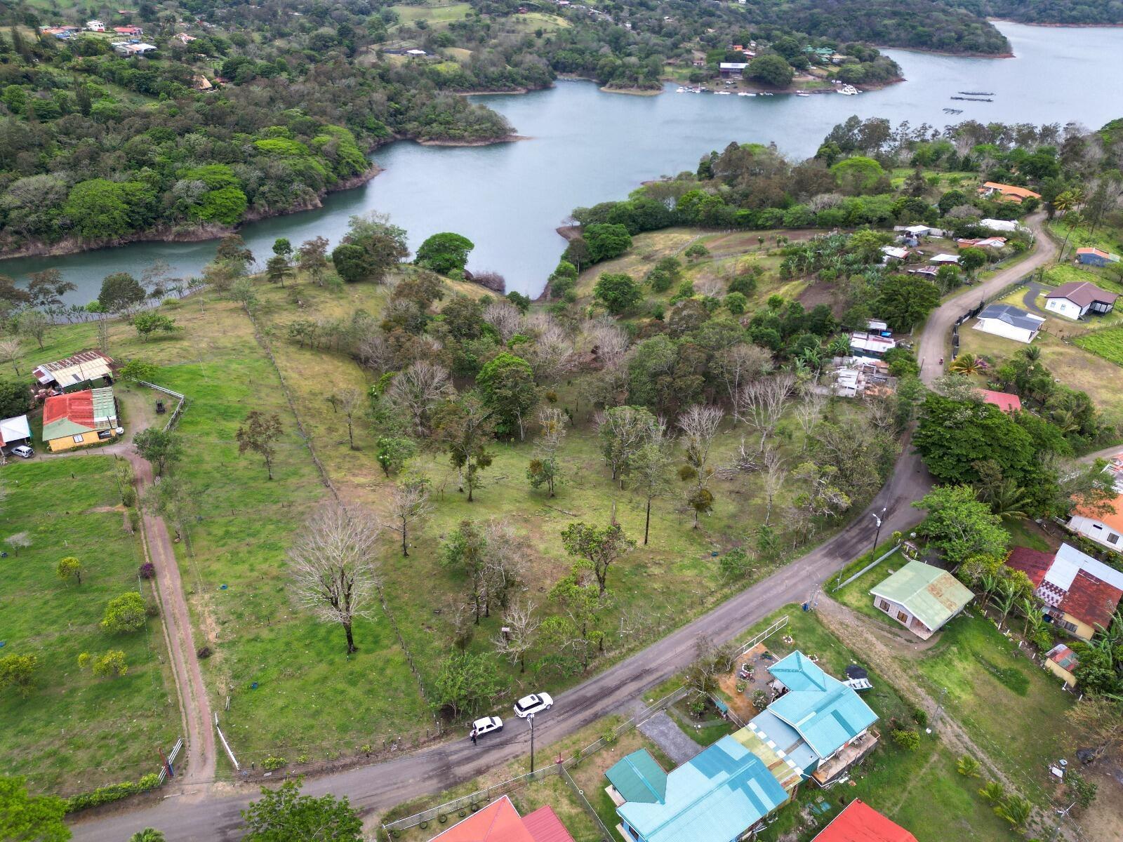 An aerial view shows a grassy lot with scattered trees near a lake and road — Lot 7 Guanacaste Province, Tronadora, FL