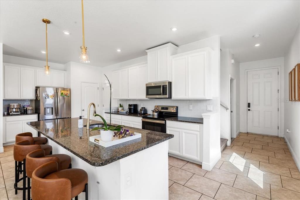 A kitchen features white cabinets, granite countertops, a center island with bar stools, and tile flooring — 2759 PLEASANT CYPRESS CIRCLE, KISSIMMEE, FL
