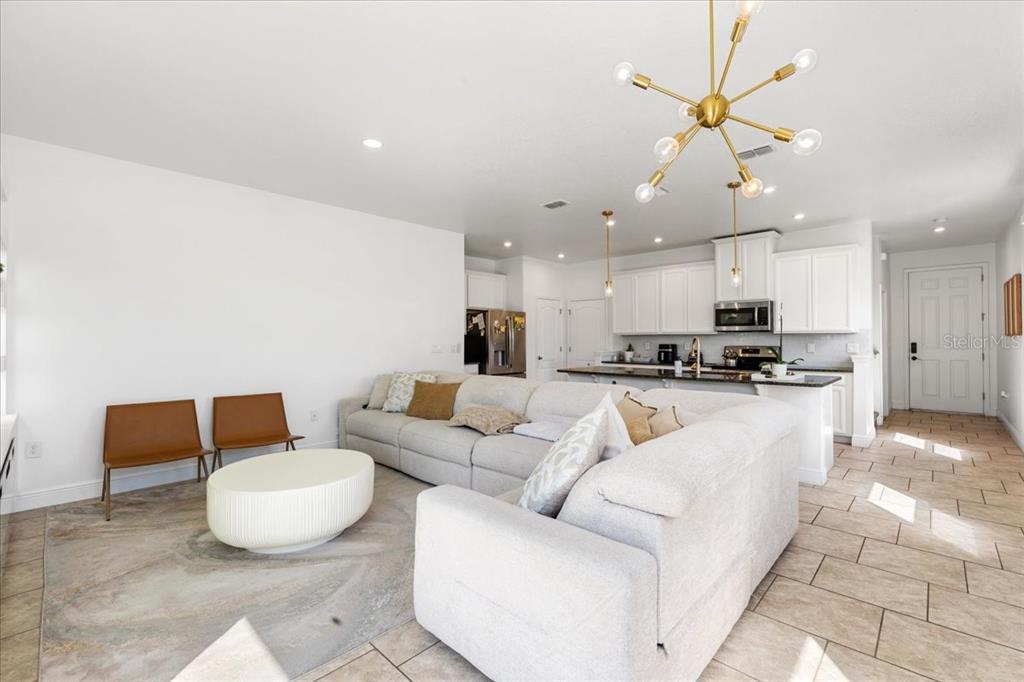 An open-concept living room and kitchen featuring a large sectional sofa and modern light fixtures — 2759 PLEASANT CYPRESS CIRCLE, KISSIMMEE, FL
