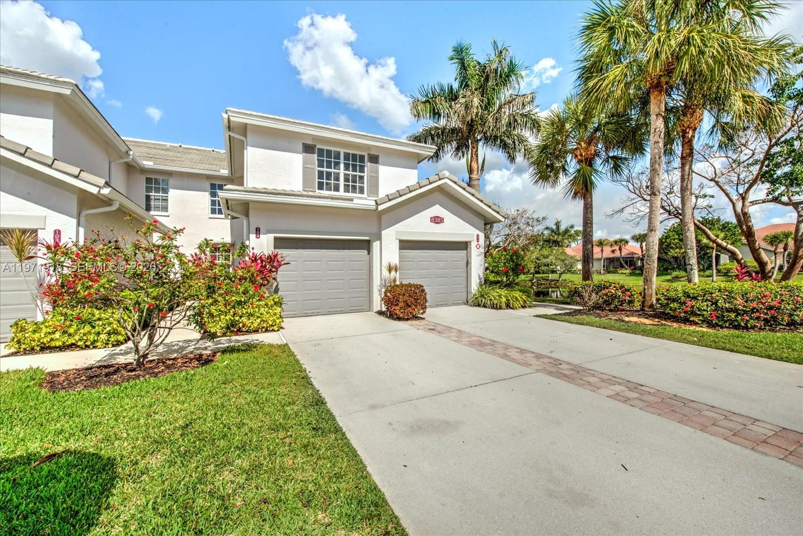 A two-story house with a two-car garage, light-colored stucco exterior, and palm trees — 8385 Whisper Trace LN Apt. # 104, Naples FL 34114, NAPLES, FL