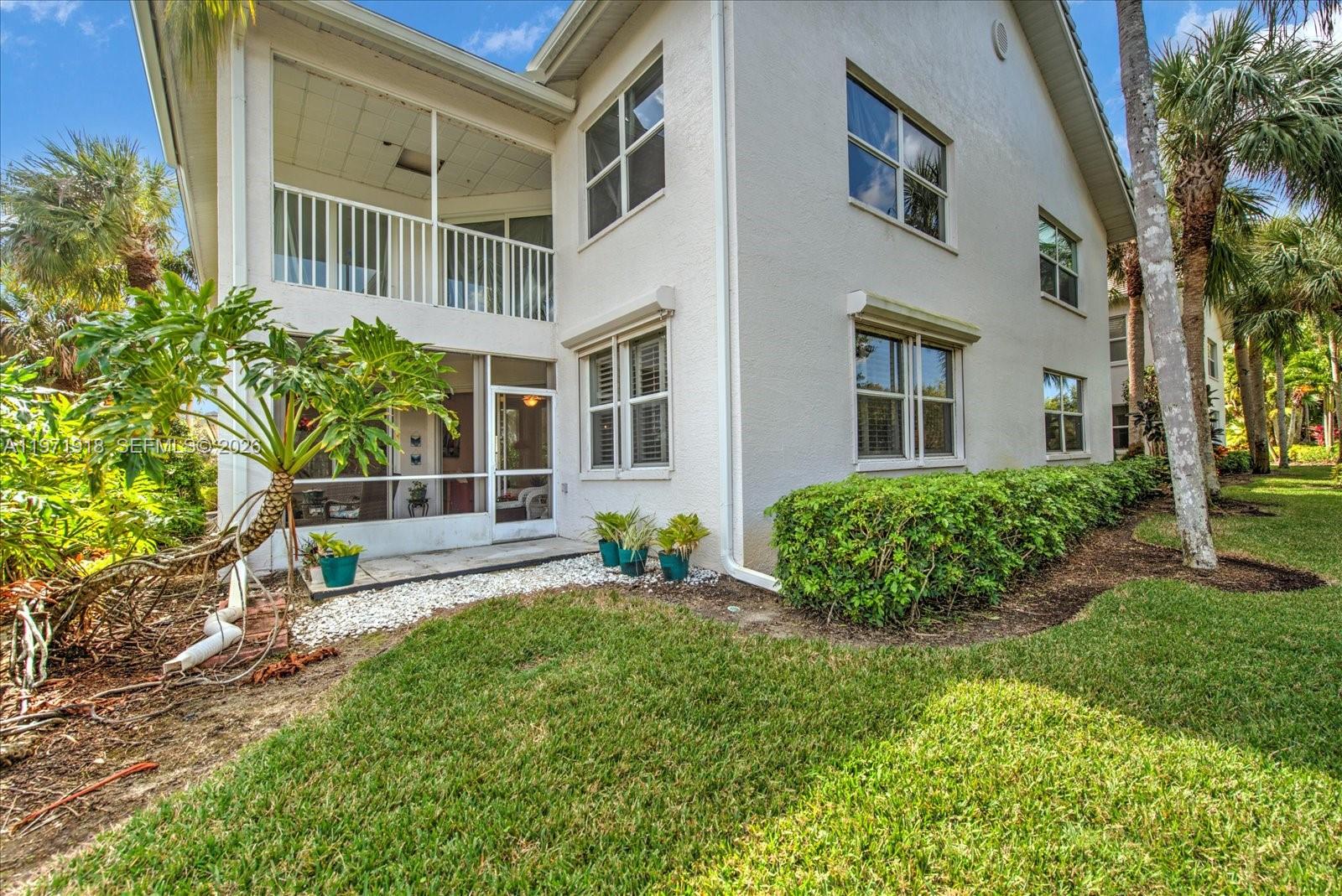 The exterior of a two-story house features a screened-in porch, white siding, and landscaping — 8385 Whisper Trace LN Apt. # 104, Naples FL 34114, NAPLES, FL