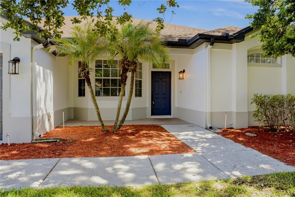 The exterior of a single-story house features a blue front door and palm trees — 1710 BROOKSTONE WAY, PLANT CITY, FL