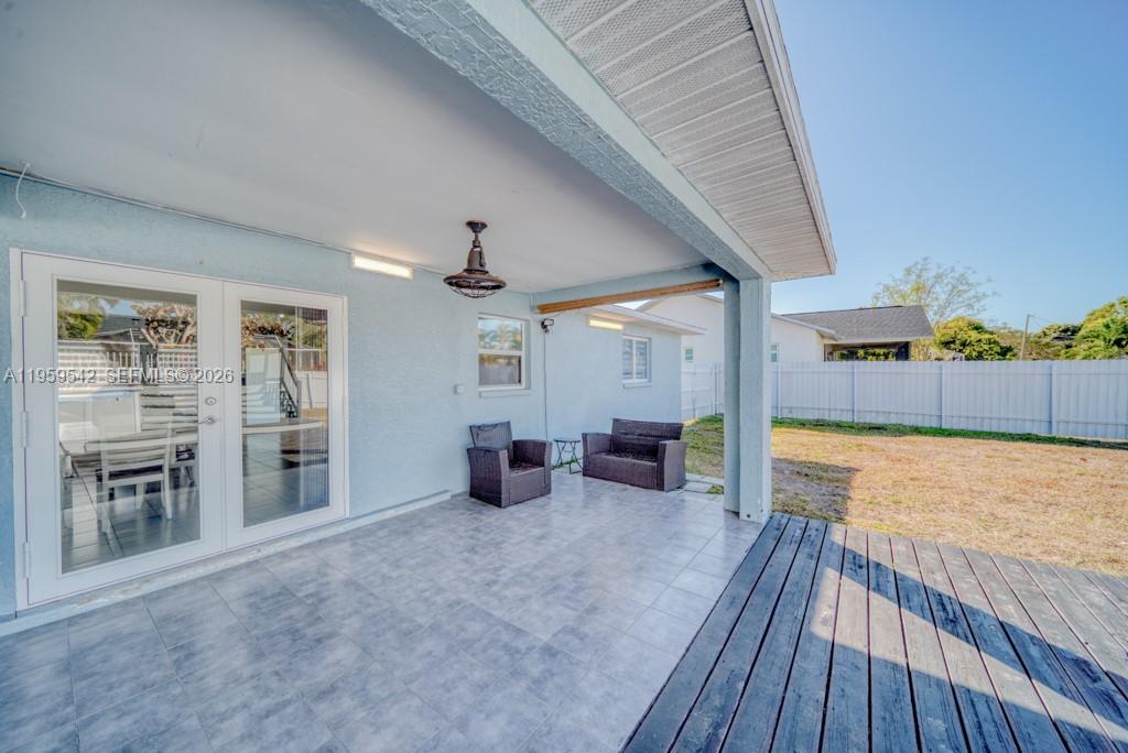A covered patio with tiled flooring, wicker furniture, and an adjacent wooden deck — 1918 SE 5th ct, Cape Coral FL 33990, CAPE CORAL, FL