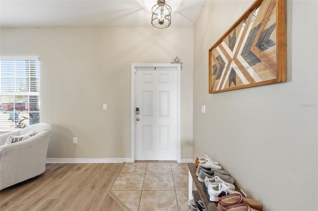 An entryway features a white front door, tile flooring, wood-look laminate, and a wall-mounted art piece — 2443 DOVESONG TRACE DRIVE, RUSKIN, FL