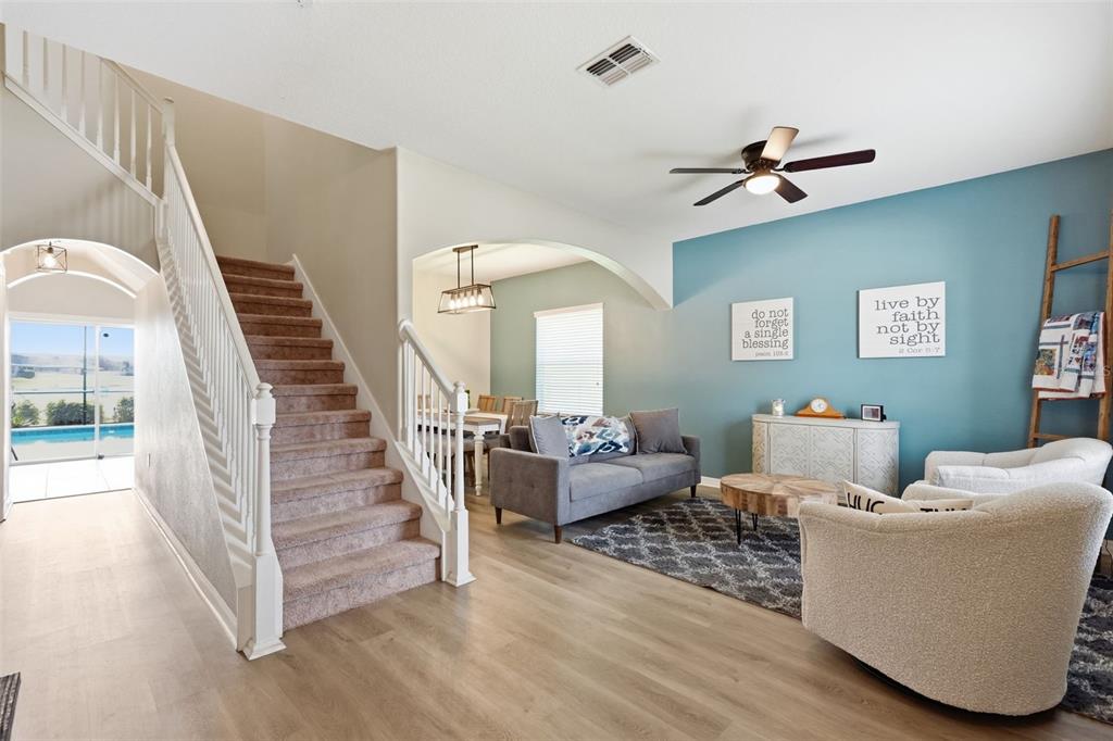 A living room with light wood floors, a staircase, and a blue accent wall — 2443 DOVESONG TRACE DRIVE, RUSKIN, FL