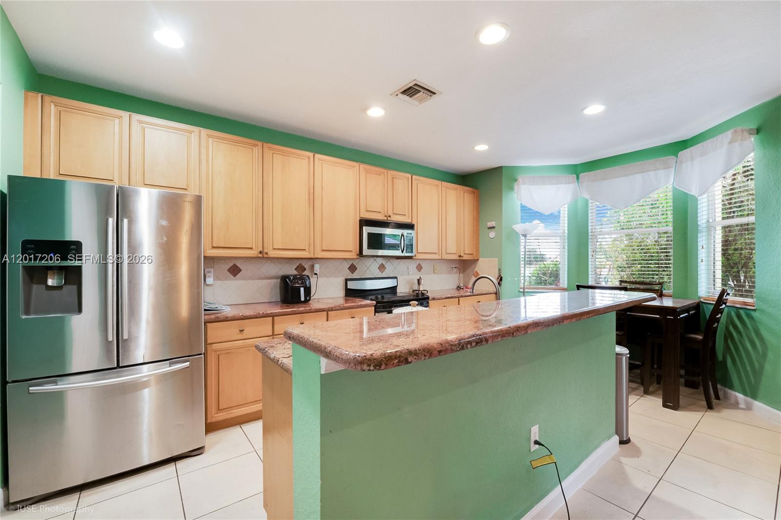 A kitchen features light wood cabinets, granite countertops, stainless steel appliances, and bright green walls — 1402 SE 16th Ave, Homestead FL 33035, HOMESTEAD, FL