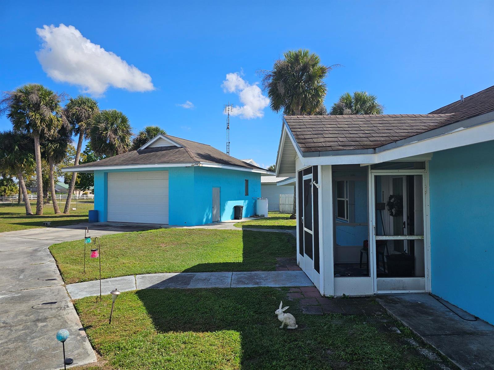 A bright blue house and detached garage sit on a grassy lot with palm trees — 13578 SW 144th Parkway, Okeechobee FL 34974, OKEECHOBEE, FL