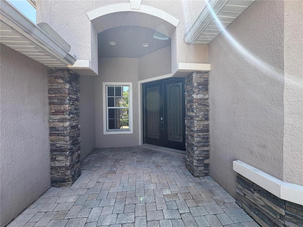 A covered entryway features stone pillars, a paver floor, and double front doors — 23307 ABERCORN LANE, LAND O LAKES, FL