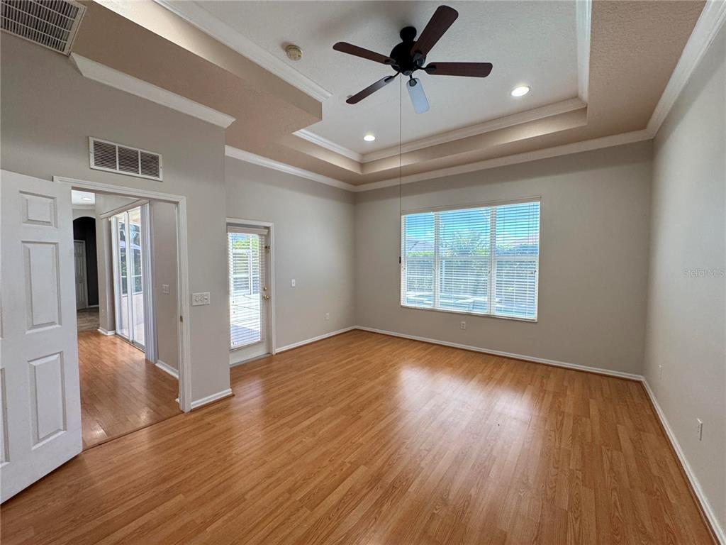 An empty room features wood-look flooring, a tray ceiling with a fan, and a glass door — 23307 ABERCORN LANE, LAND O LAKES, FL