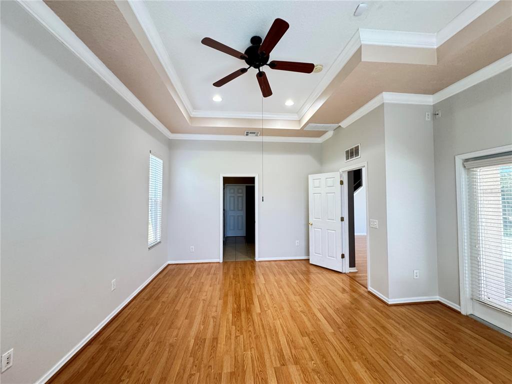 An empty room features hardwood floors, a tray ceiling with a fan, and white walls — 23307 ABERCORN LANE, LAND O LAKES, FL