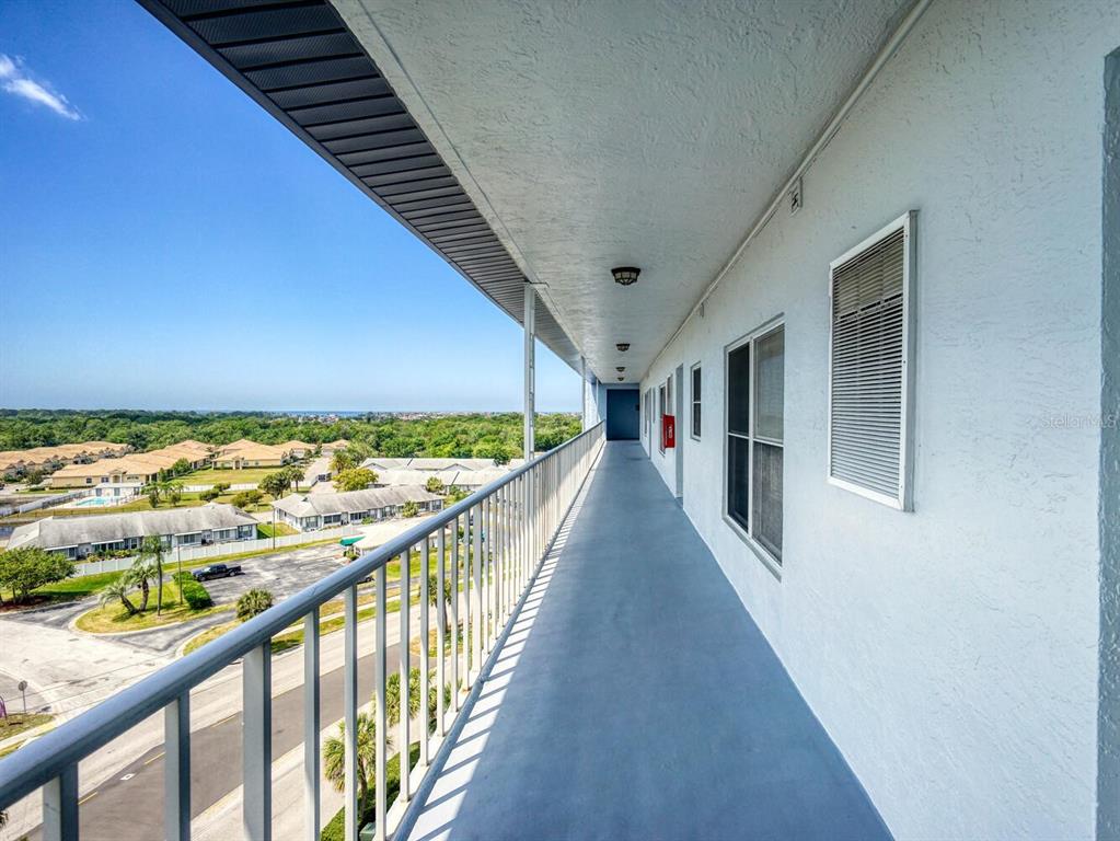 An outdoor balcony walkway overlooks a residential neighborhood with a view of the distant ocean — 4939 FLORAMAR TERRACE UNIT 912, NEW PORT RICHEY, FL