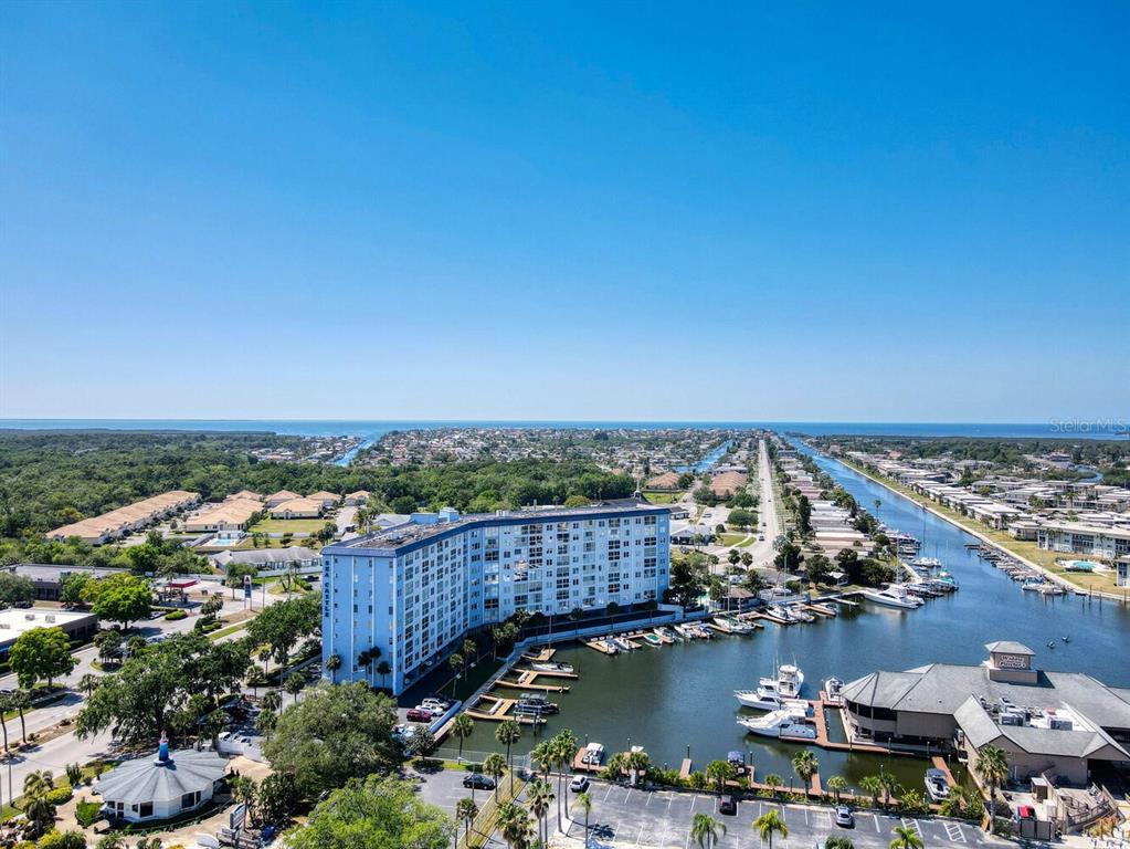 An aerial view shows a multi-story apartment building situated along a canal with docked boats — 4939 FLORAMAR TERRACE UNIT 912, NEW PORT RICHEY, FL