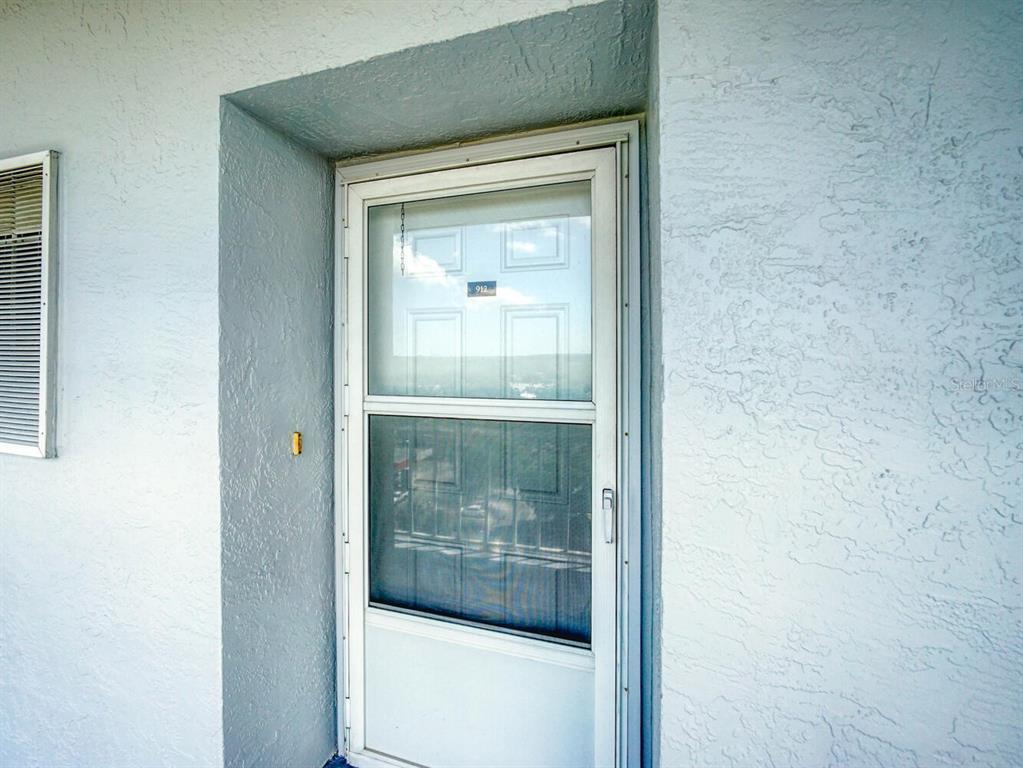 A white storm door with a glass panel is set into a textured exterior wall — 4939 FLORAMAR TERRACE UNIT 912, NEW PORT RICHEY, FL