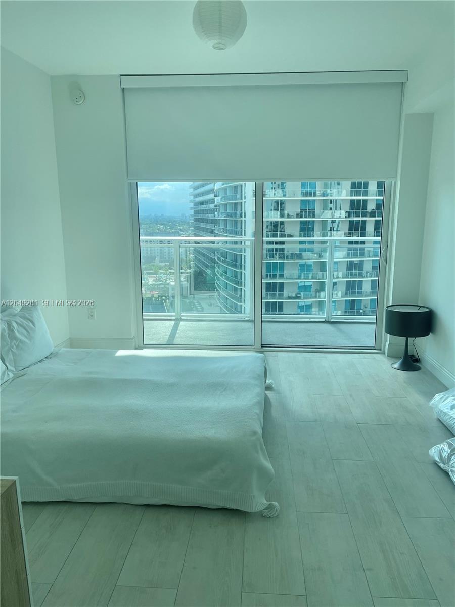 A bedroom features a bed, light-colored wood-look flooring, and a sliding glass door to a balcony — 1080 Brickell Ave # 1709, Miami FL 33131, MIAMI, FL