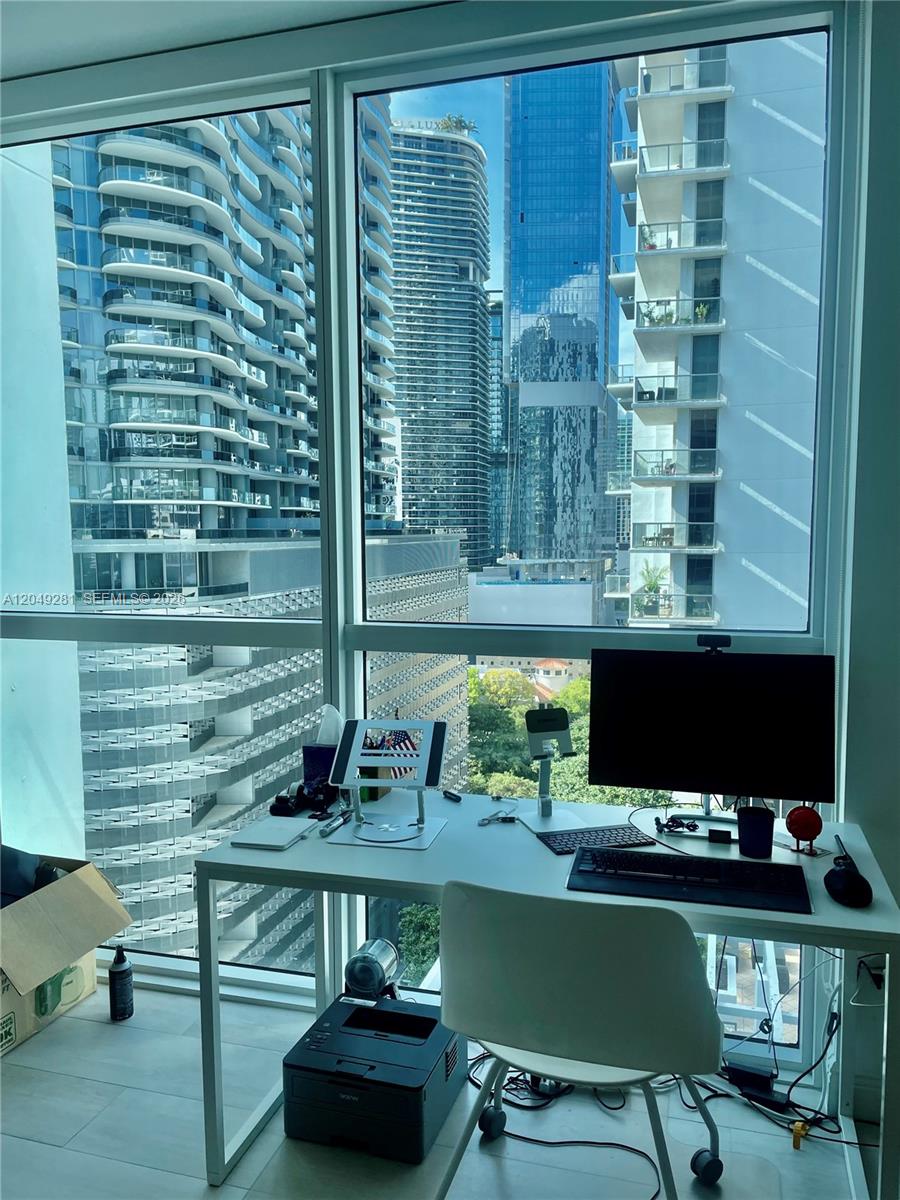 A home office features a white desk and chair positioned before floor-to-ceiling windows overlooking skyscrapers — 1080 Brickell Ave # 1709, Miami FL 33131, MIAMI, FL