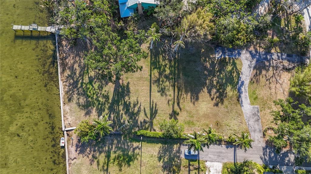 An aerial view shows a vacant waterfront lot with a private dock and paved driveway — 408 31ST STREET NW, BRADENTON, FL