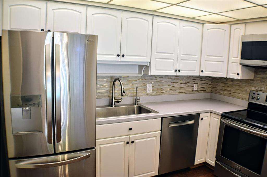 A kitchen features white cabinets, stainless steel appliances, a tiled backsplash, and gray countertops — 814 PARK LAKE CIRCLE UNIT 8, MAITLAND, FL