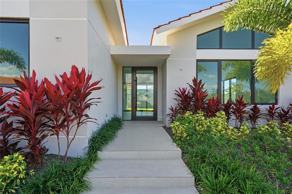 A modern home entrance features a glass front door, concrete steps, and lush tropical landscaping — 804 CAMINO DE LAS VERBENAS, DORADO, PR