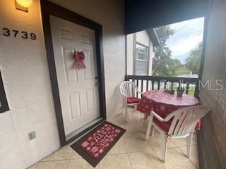 A covered patio features a white front door, tiled flooring, and a small bistro set — 3739 59TH AVENUE W UNIT 3739, BRADENTON, FL