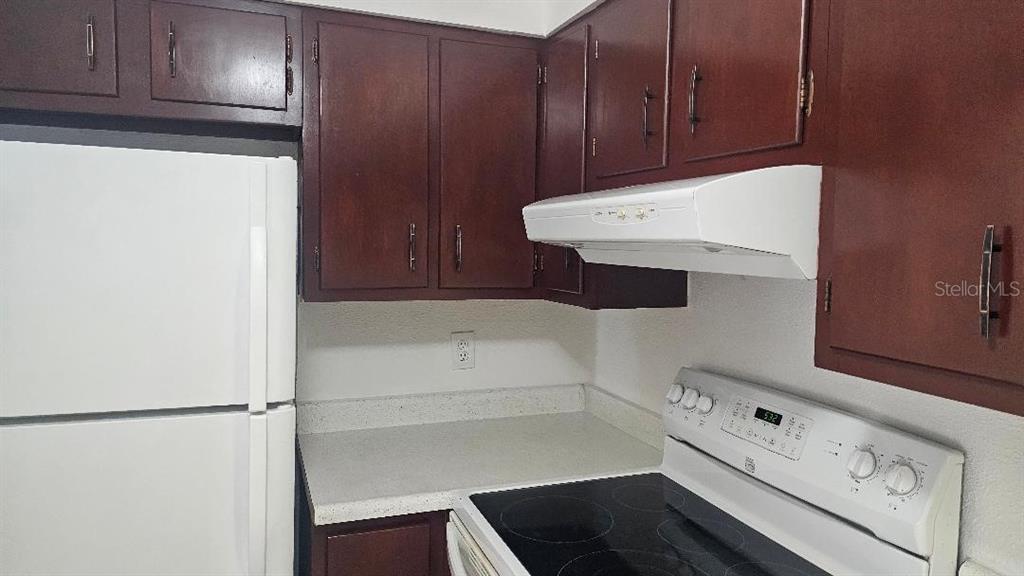 A kitchen features dark wood cabinets, white appliances, and a light-colored countertop — 10365 PARADISE BOULEVARD UNIT 10, TREASURE ISLAND, FL