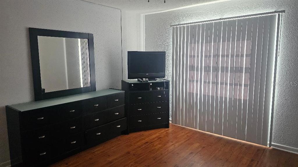 A bedroom features dark wood furniture, a mirror, and vertical blinds covering a sliding glass door — 10365 PARADISE BOULEVARD UNIT 10, TREASURE ISLAND, FL