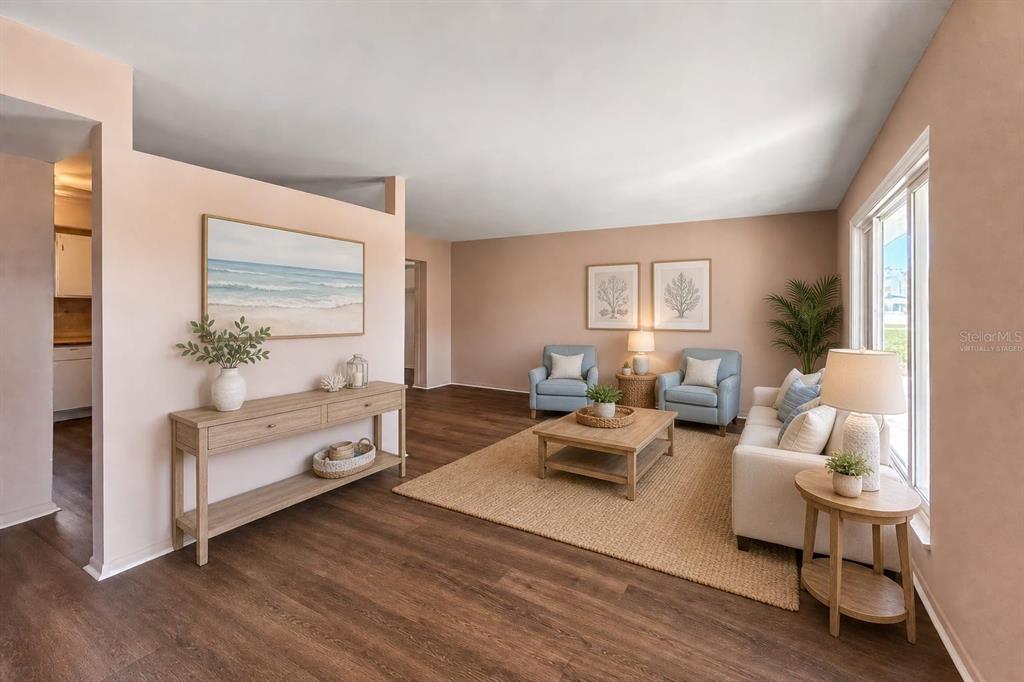 This virtually staged living room features light-colored walls, wood-look flooring, and a neutral area rug — 1515 ARROWHEAD DRIVE, SUN CITY CENTER, FL