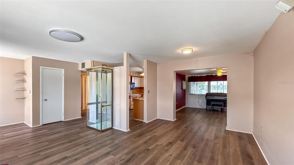 A living area with wood-look flooring, a glass display cabinet, and an adjacent kitchen — 1515 ARROWHEAD DRIVE, SUN CITY CENTER, FL