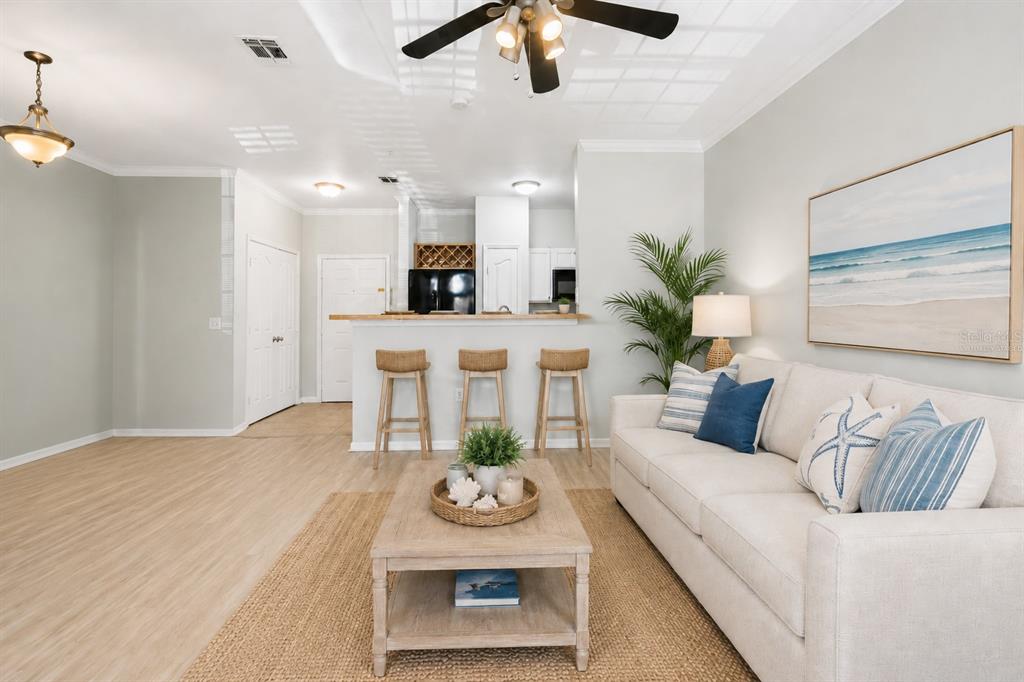 A living room with light wood floors, a beige sofa, and a breakfast bar area — 5000 CULBREATH KEY WAY UNIT 1-107, TAMPA, FL