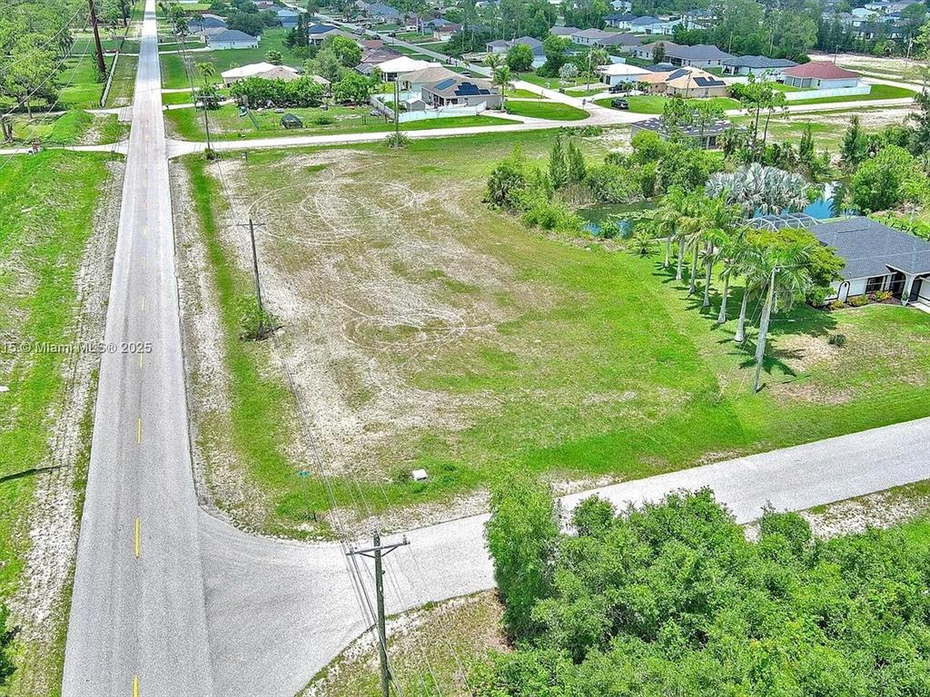 An aerial view shows a vacant, grassy lot situated between a road and a pond — 3417 ANDALUSIA BOULEVARD, CAPE CORAL, FL