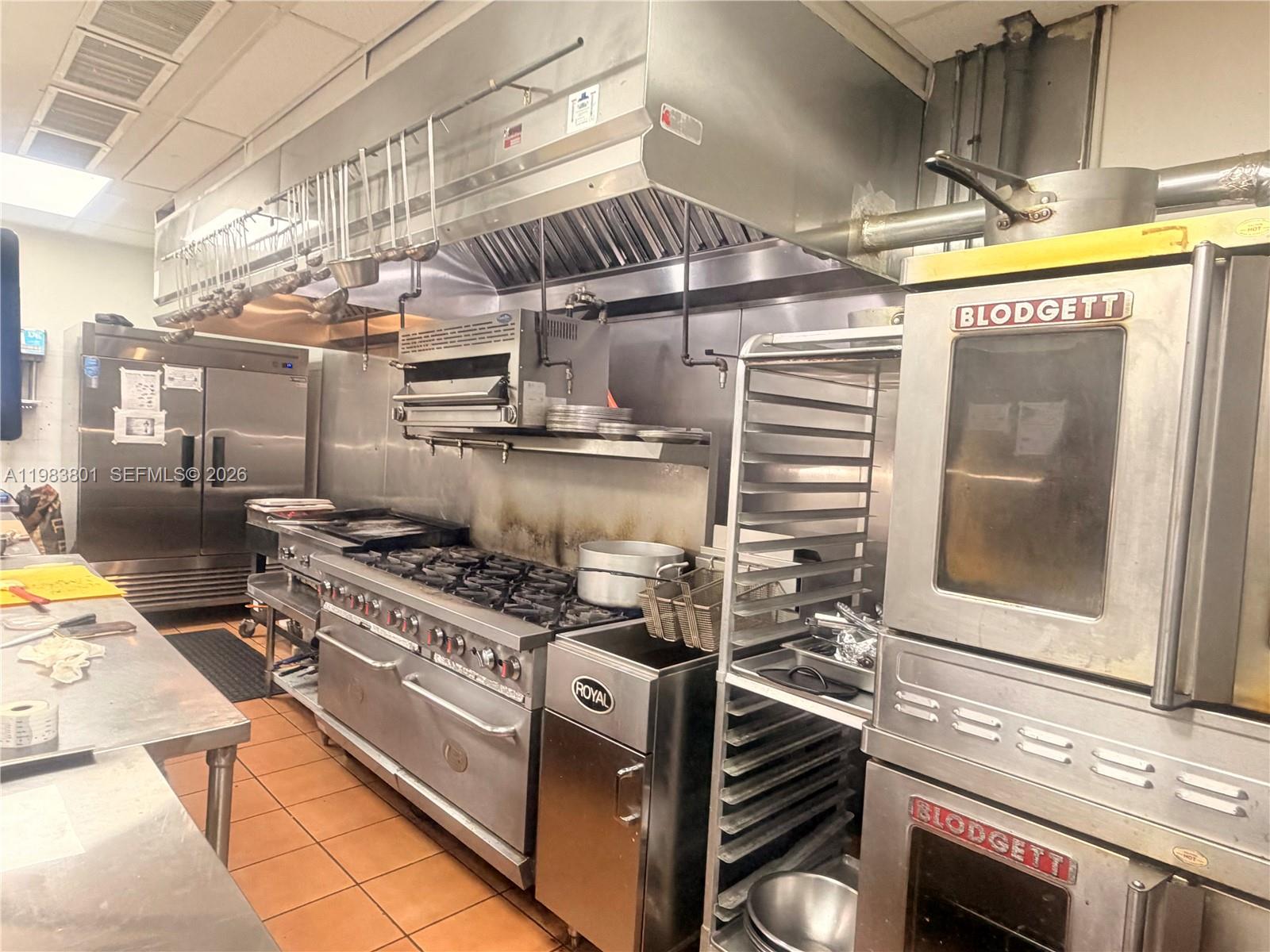 A commercial kitchen features stainless steel appliances, a large exhaust hood, and tiled flooring — SUNNY ISLES BEACH, FL