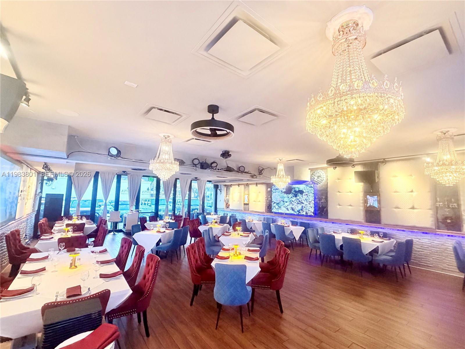 A restaurant dining room features multiple crystal chandeliers, upholstered chairs, and white-clothed tables — SUNNY ISLES BEACH, FL
