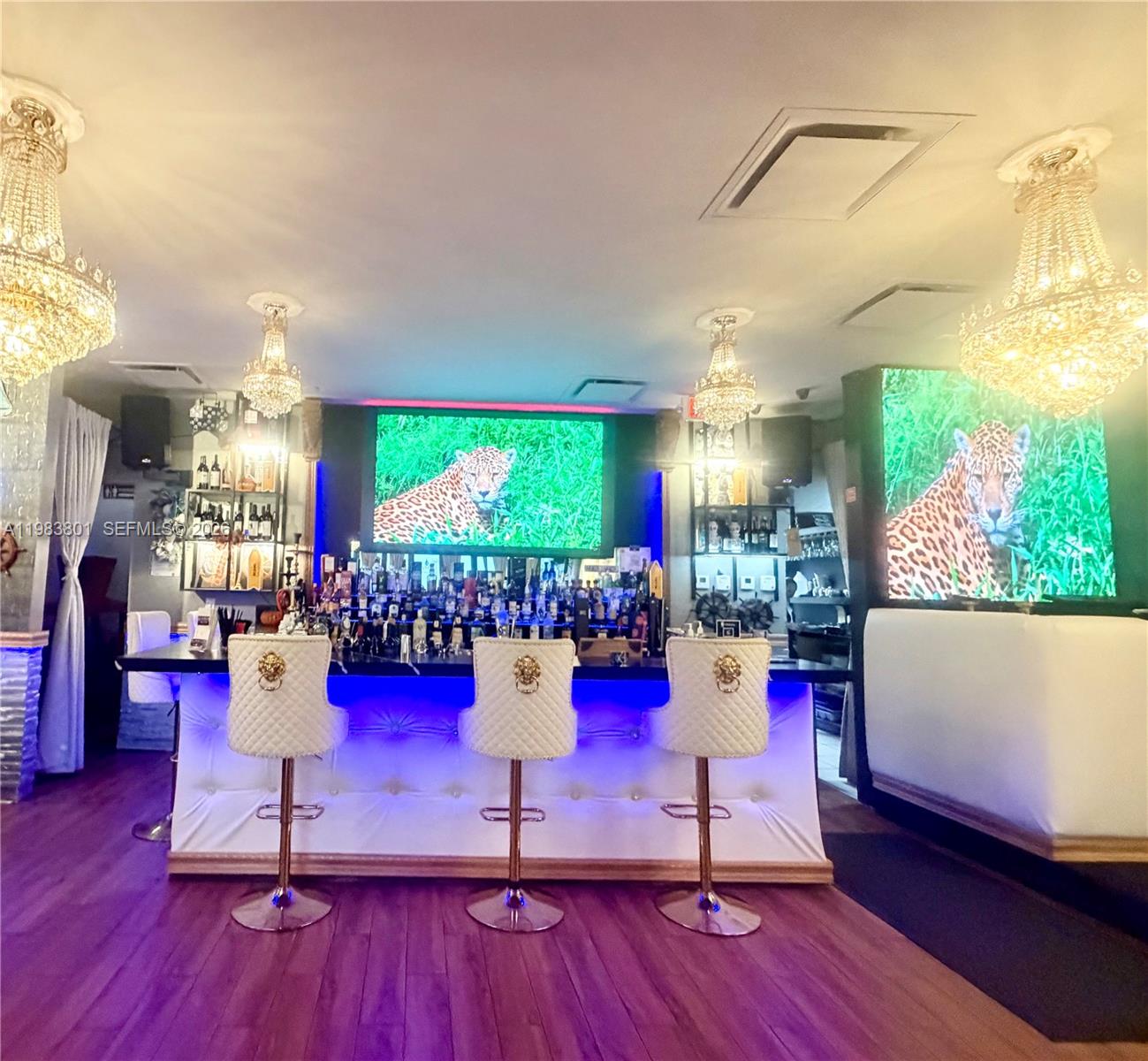 A bar area features three white tufted stools, crystal chandeliers, and leopard-themed wall art — SUNNY ISLES BEACH, FL