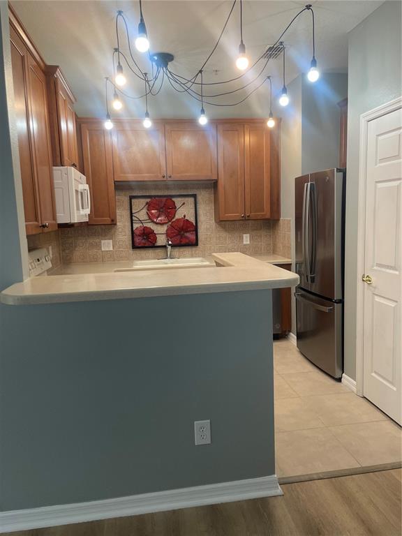 A kitchen features wood cabinets, a breakfast bar, stainless steel appliances, and a spider chandelier — 10092 REGENT PARK DRIVE UNIT 2301, ORLANDO, FL