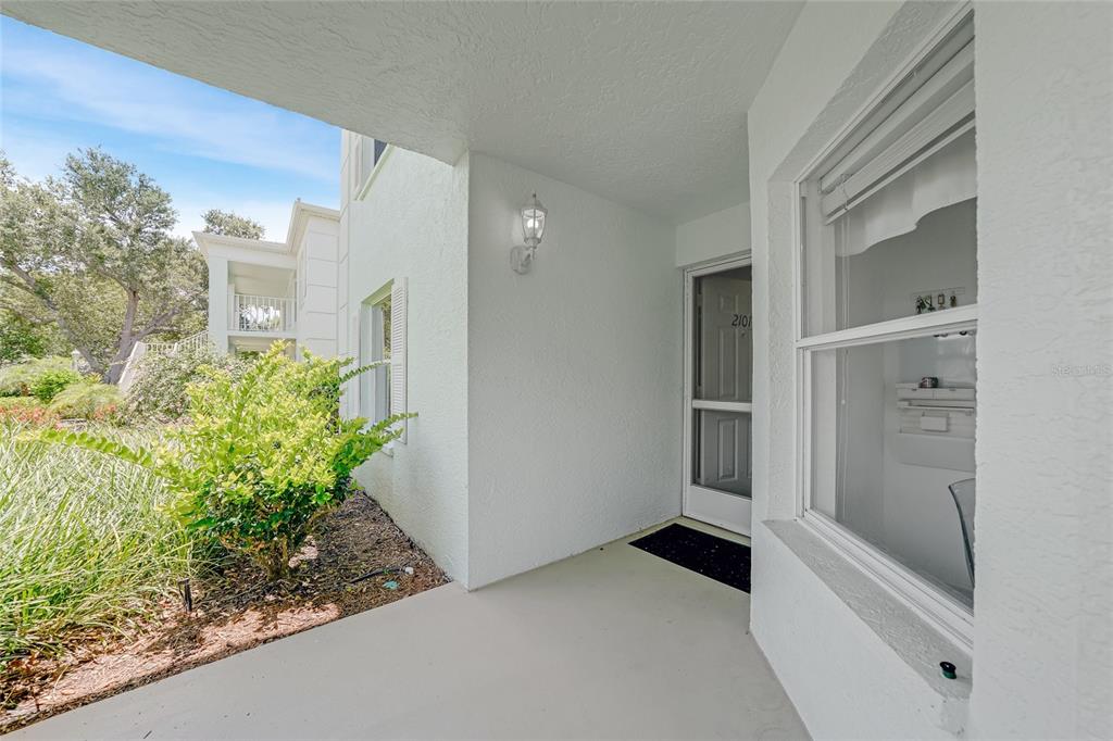 A covered entryway features a white door with a screen, a window, and landscaping — 5725 GREENWOOD AVENUE UNIT 2101, NORTH PORT, FL