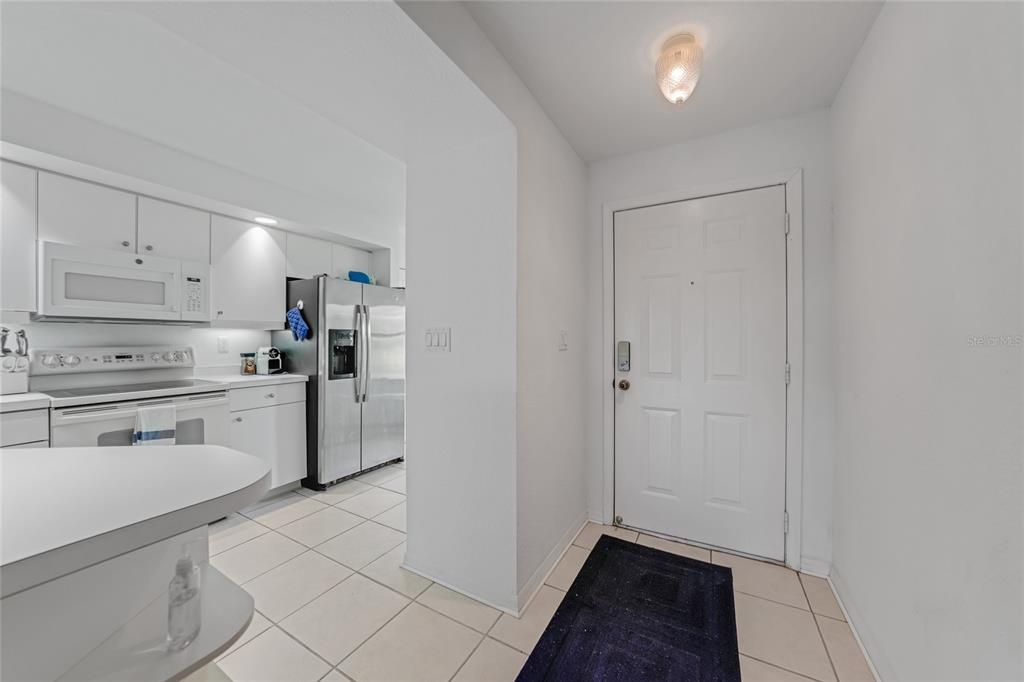 A white kitchen with stainless steel appliances is visible from an entryway with tile floors — 5725 GREENWOOD AVENUE UNIT 2101, NORTH PORT, FL