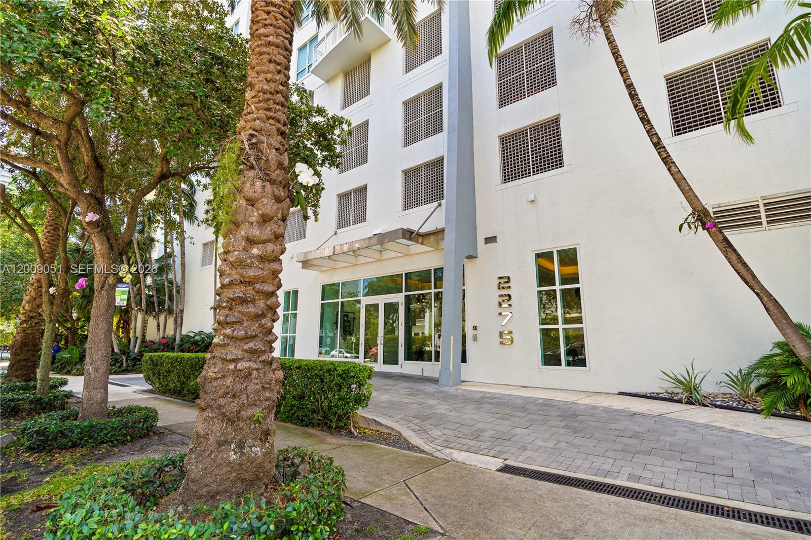 The exterior of a multi-story white building features a glass entrance and palm trees — 2275 Biscayne Blvd # 802, Miami FL 33137, MIAMI, FL