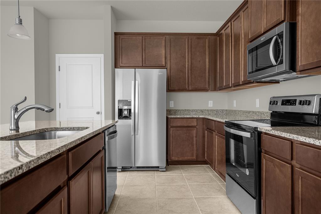 A kitchen features dark wood cabinets, granite countertops, stainless steel appliances, and tile flooring — 1927 HOLDEN RIDGE LANE, CLERMONT, FL
