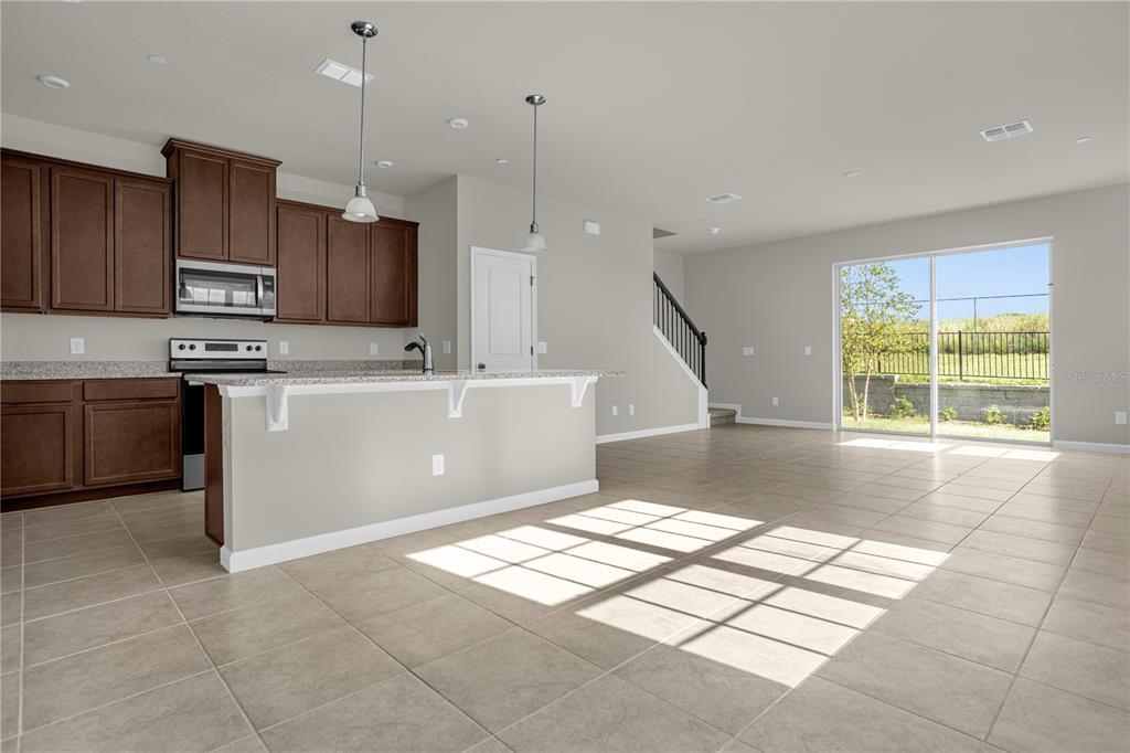 An open-concept kitchen with dark wood cabinets and a breakfast bar overlooks a living area — 1927 HOLDEN RIDGE LANE, CLERMONT, FL