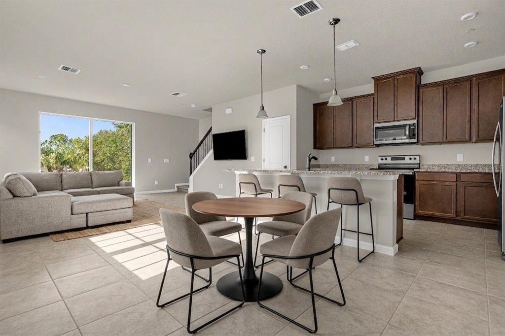 An open-concept kitchen and living area features dark wood cabinets, tile flooring, and a dining table — 1927 HOLDEN RIDGE LANE, CLERMONT, FL